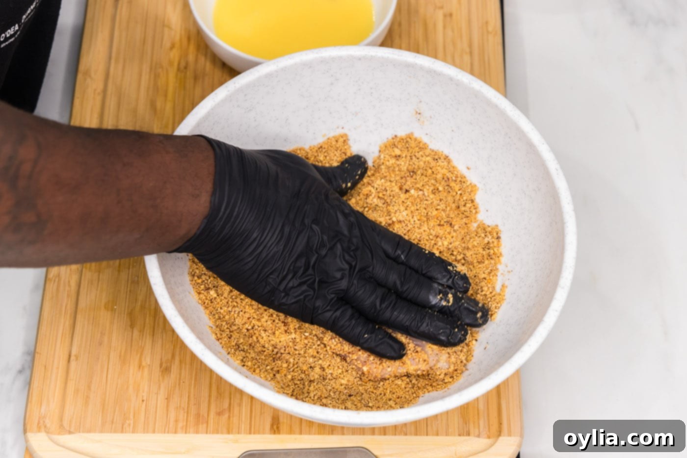 hand patting chicken breast with almond breading