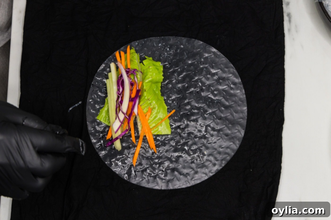 carrots, lettuce, and cabbage being added to a soft spring roll wrapper