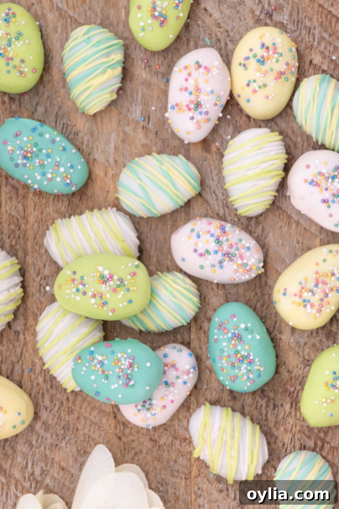 Assorted Easter Egg Oreo Truffles on a wooden board, decorated with drizzles and sprinkles