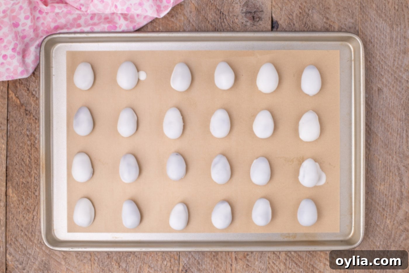 White chocolate coated egg shaped Oreo balls drying on parchment paper