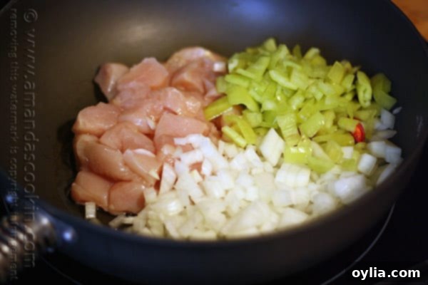 A close-up photo of cubed chicken, vibrant banana peppers, and diced onions cooking in a skillet.