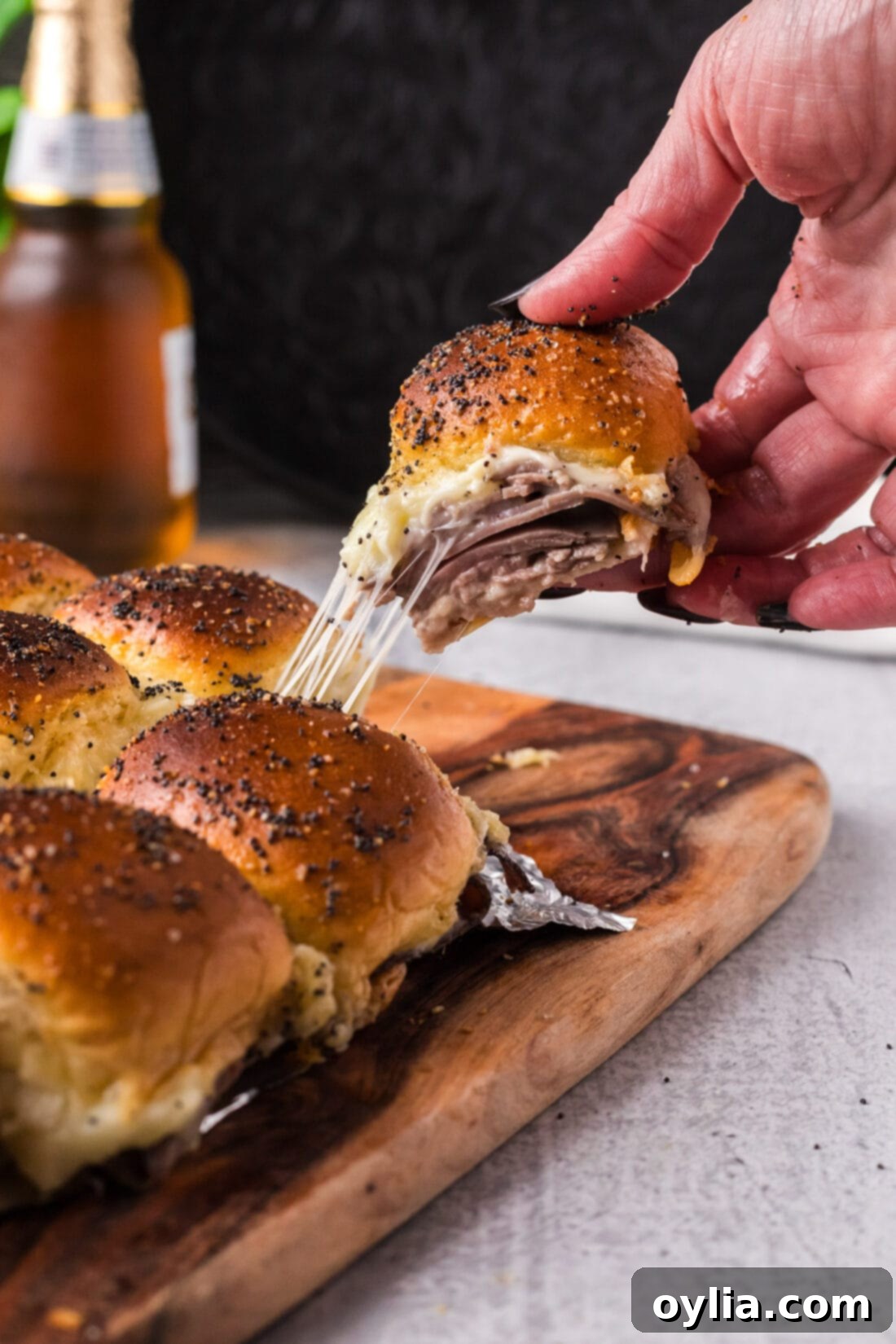 Hand pulling up a Roast Beef Slider from a board with a cheese pull