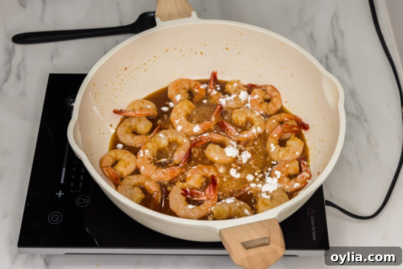 cornstarch sprinkled over honey garlic shrimp in a skillet