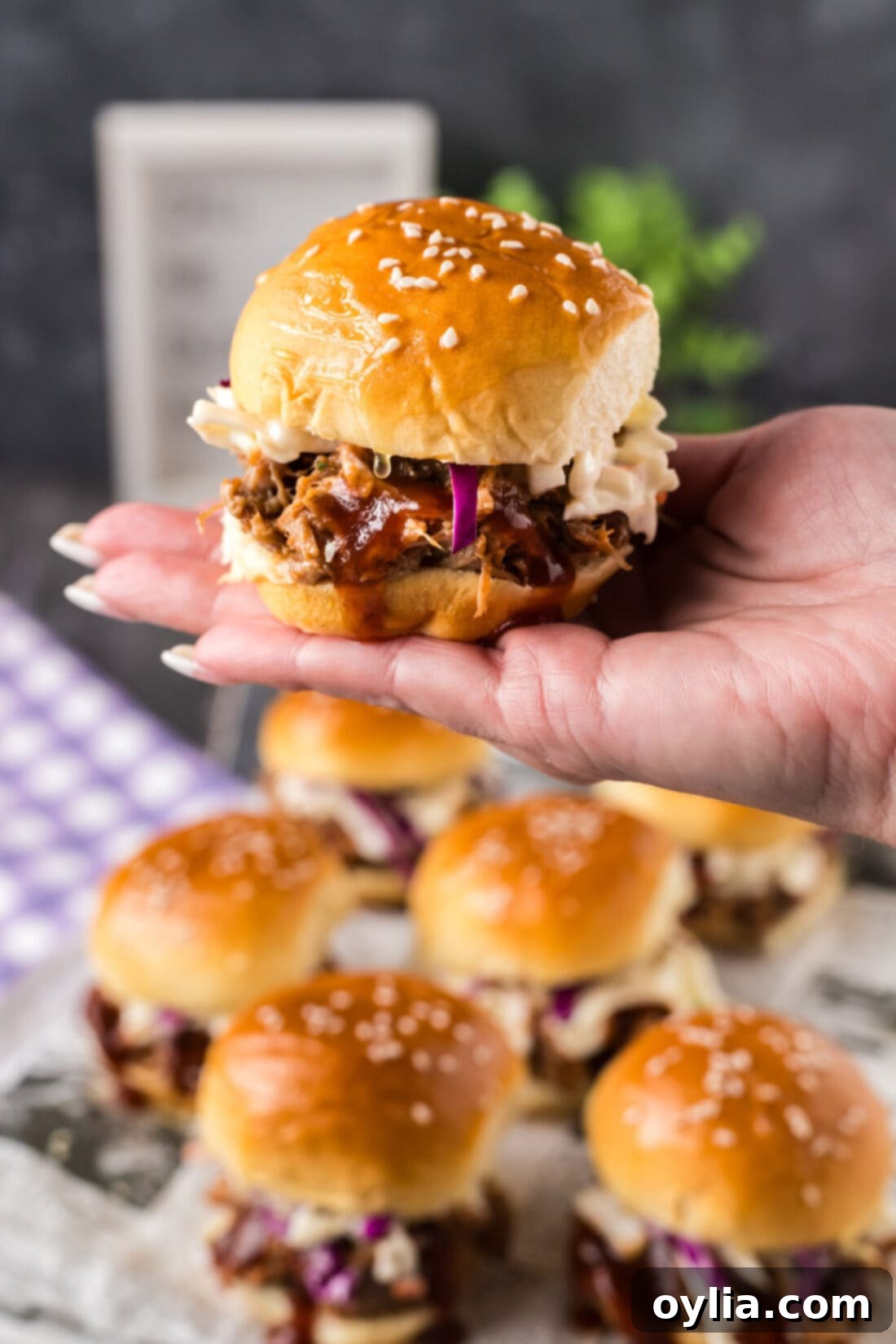Hand holding up a Pulled Pork Slider over more Pulled Pork Sliders, showcasing their delicious appeal