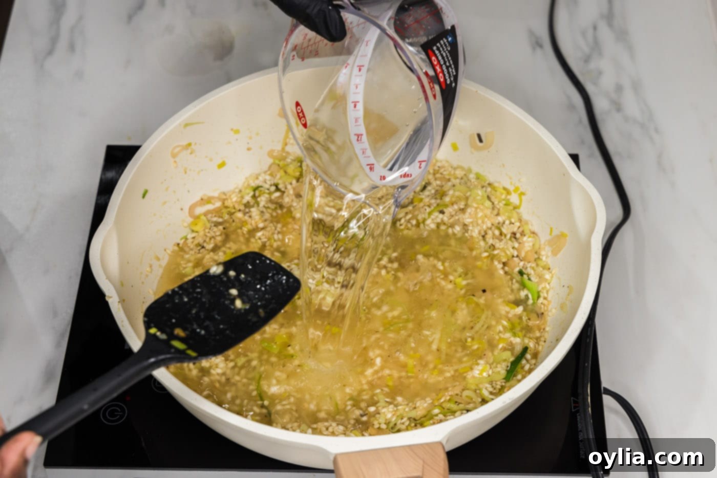 pouring water into risotto in a skillet