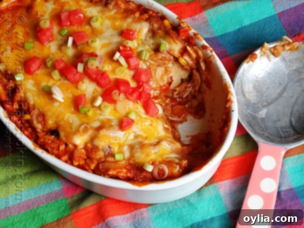 An overhead photo of a chicken tostada casserole with chopped green onions and tomatoes on top with a serving missing.