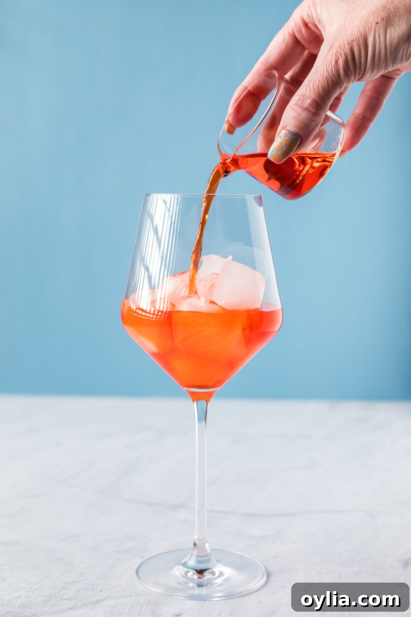 pouring Aperol into a wine glass with ice