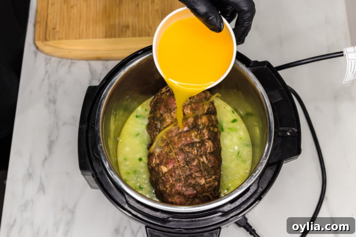 Pouring fresh orange juice directly over the pork roast, jalapeno, and onion in the Instant Pot.