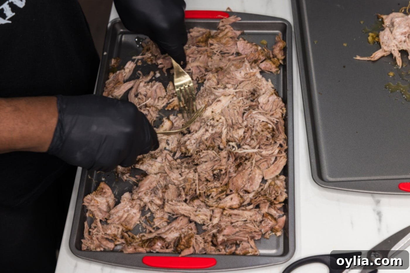 Using two forks to effortlessly shred the tender pork carnitas on a baking sheet.
