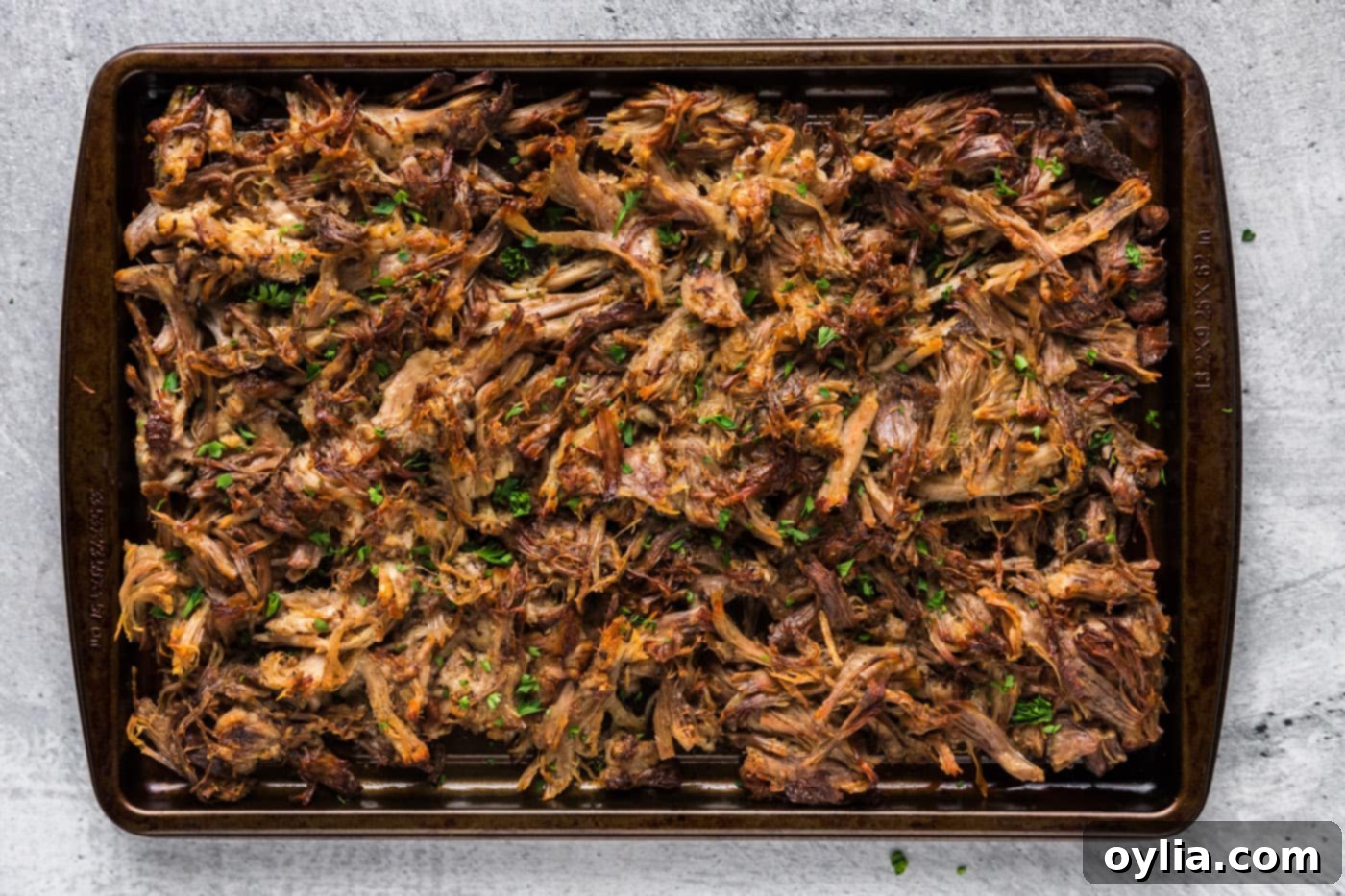 Perfectly shredded Instant Pot Carnitas with beautifully crispy edges after being broiled, spread out on a baking sheet.