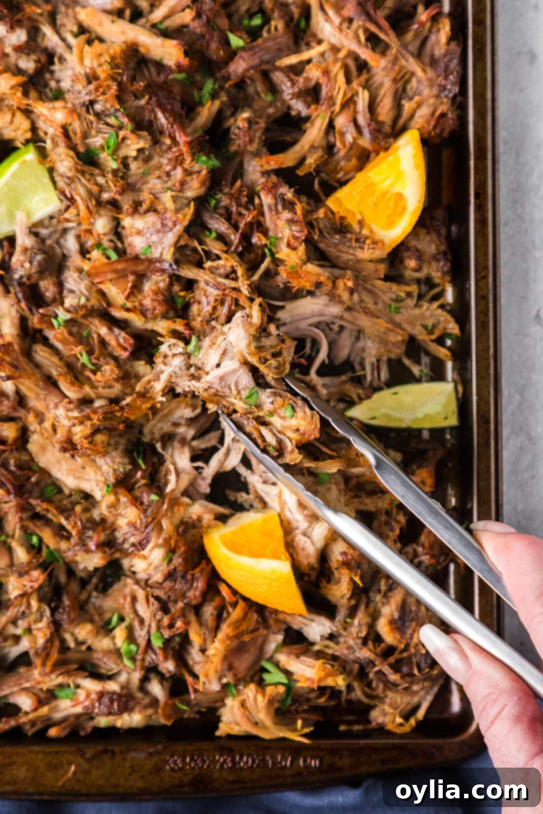 Crispy Instant Pot Carnitas 3 Tongs picking up crispy Instant Pot Carnitas from a sheet pan, ready to serve.
