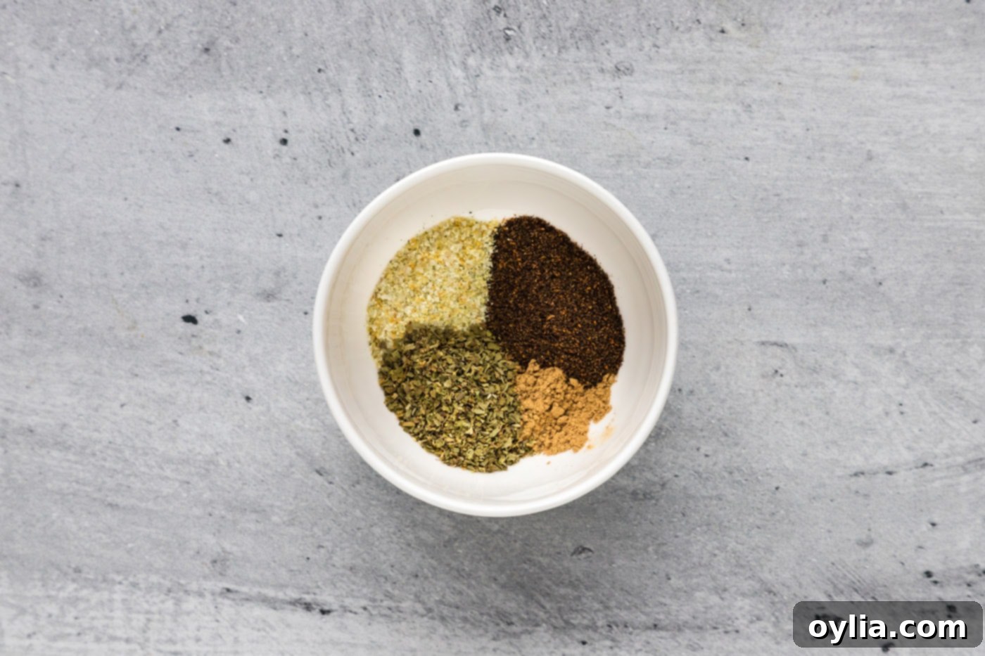 A small bowl containing a vibrant mix of chili powder, dried oregano, ground cumin, and garlic salt, ready for the pork.