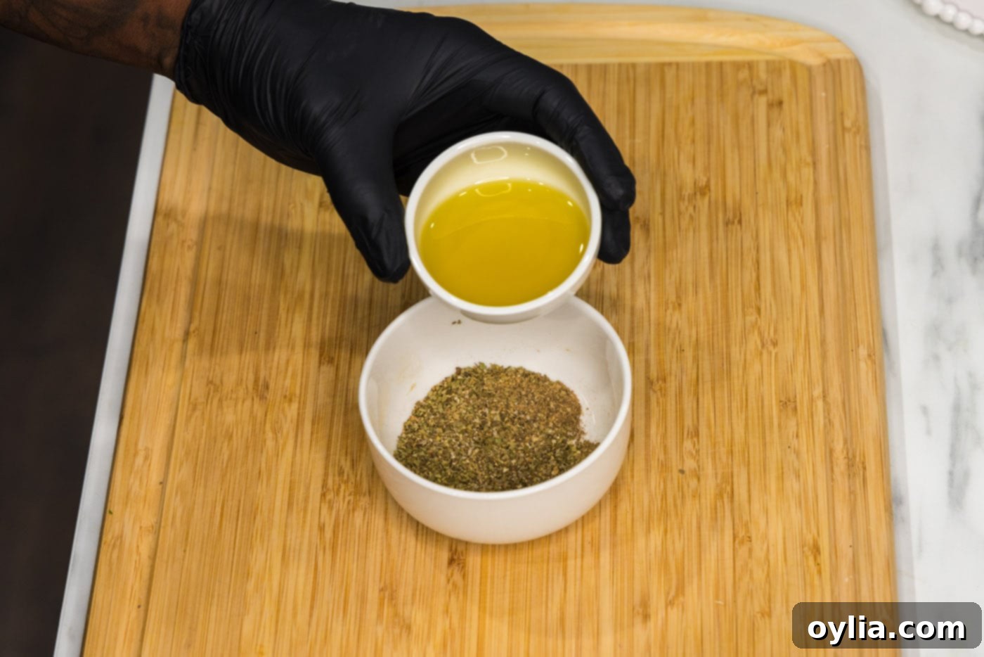 Adding olive oil to the bowl of spices, forming a thick paste for the pork rub.