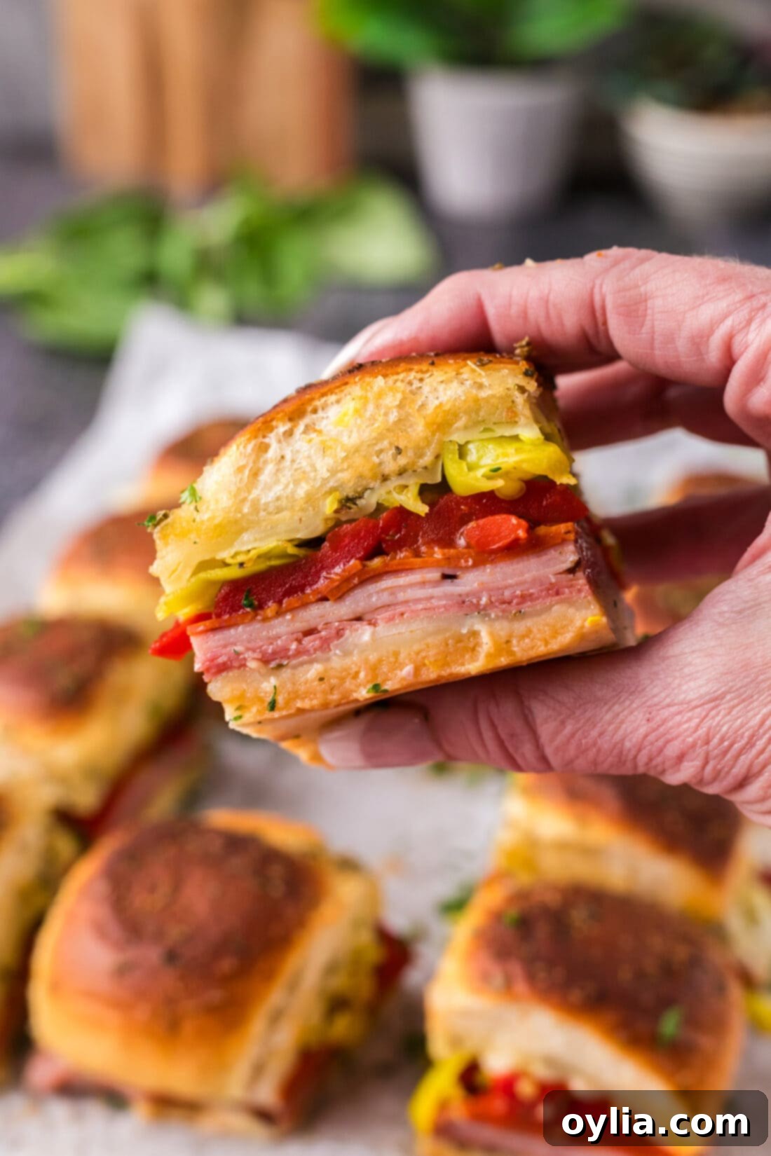 Hand holding up an Italian Slider with melted cheese and deli meats