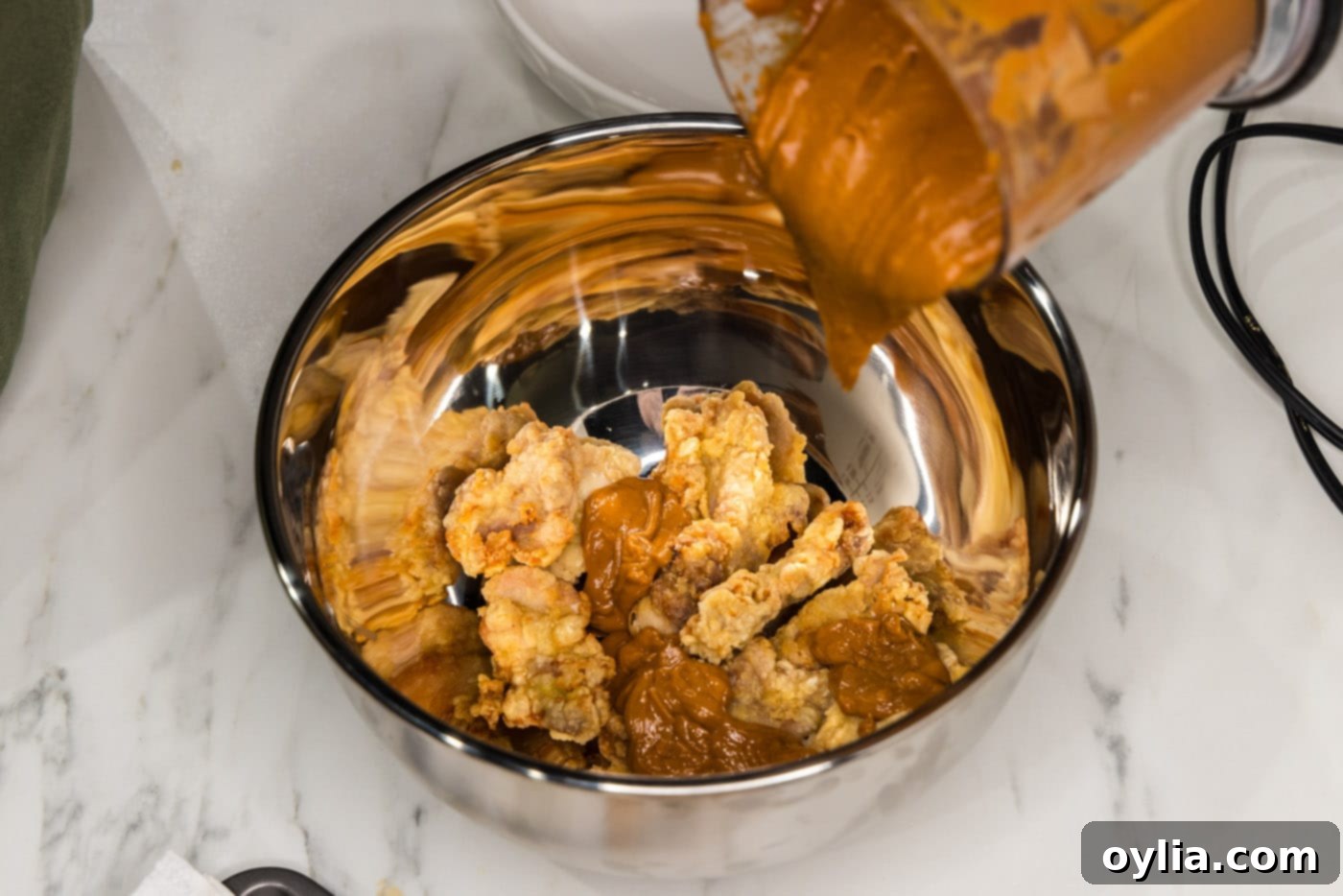 pouring peanut butter sauce over fried chicken