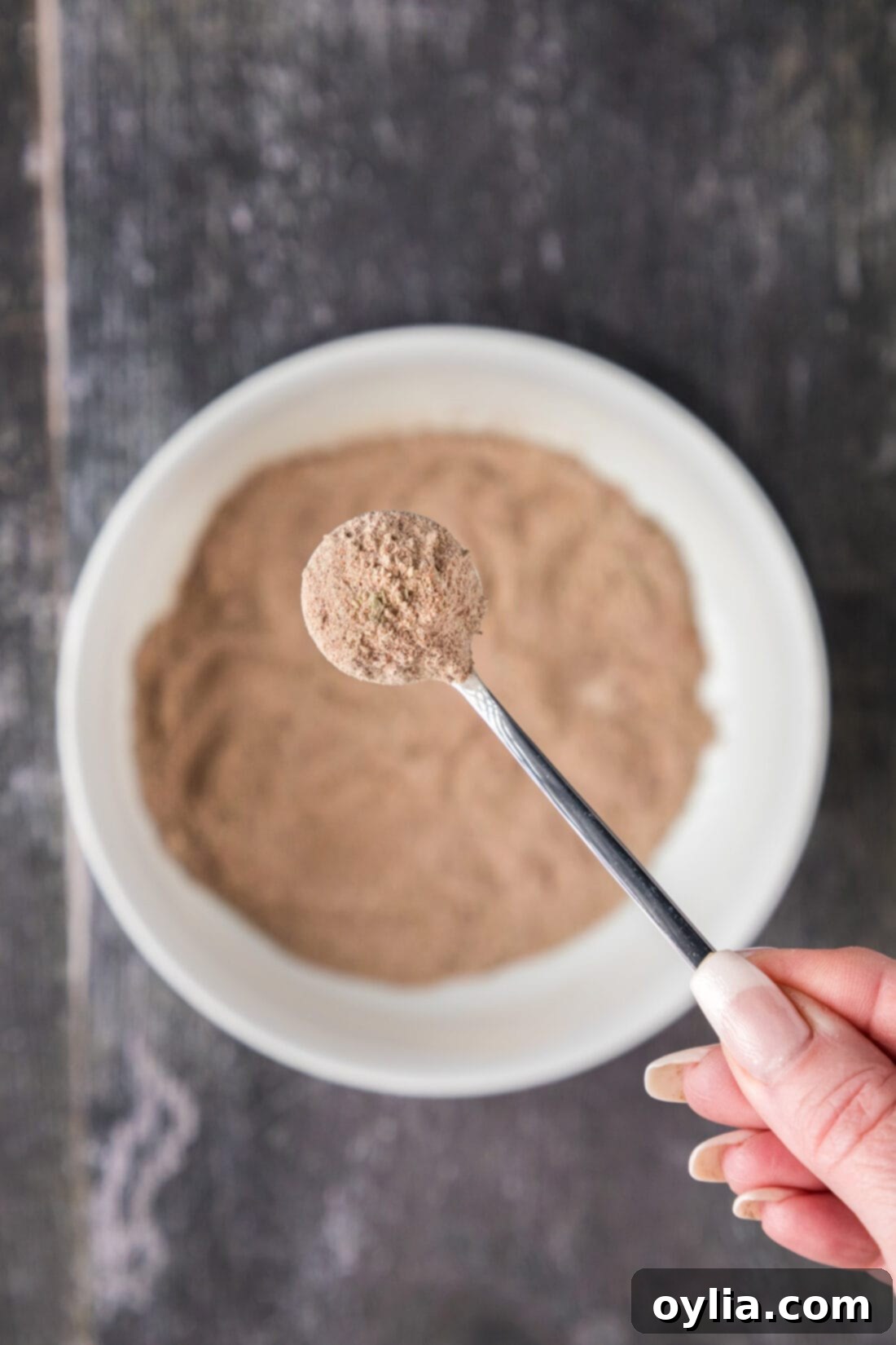 Spoonful of Mexican Seasoning held above a bowl of Mexican Seasoning
