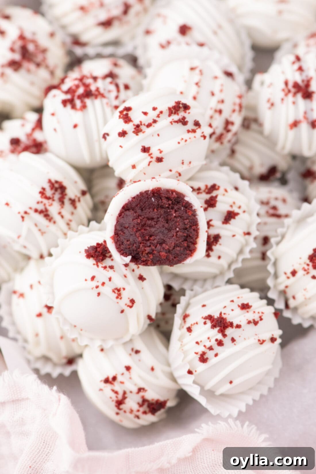 Decadent Red Velvet Cake Balls, with one cut in half revealing moist cake and frosting, resting on top of whole cake balls