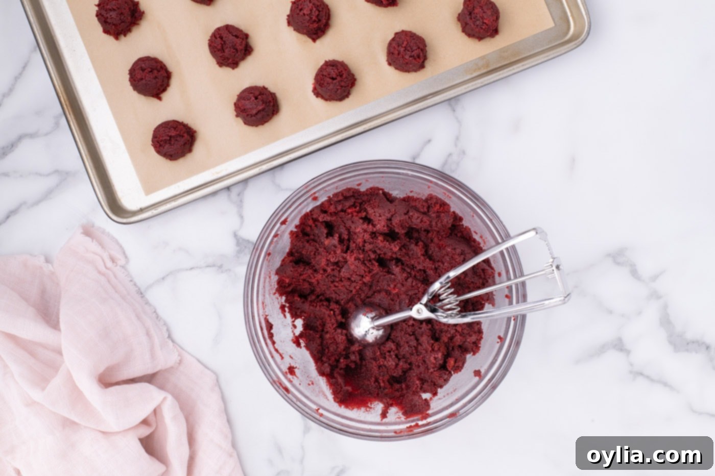 Cookie dough scoop with red velvet cake ball mixture, next to perfectly rolled cake balls