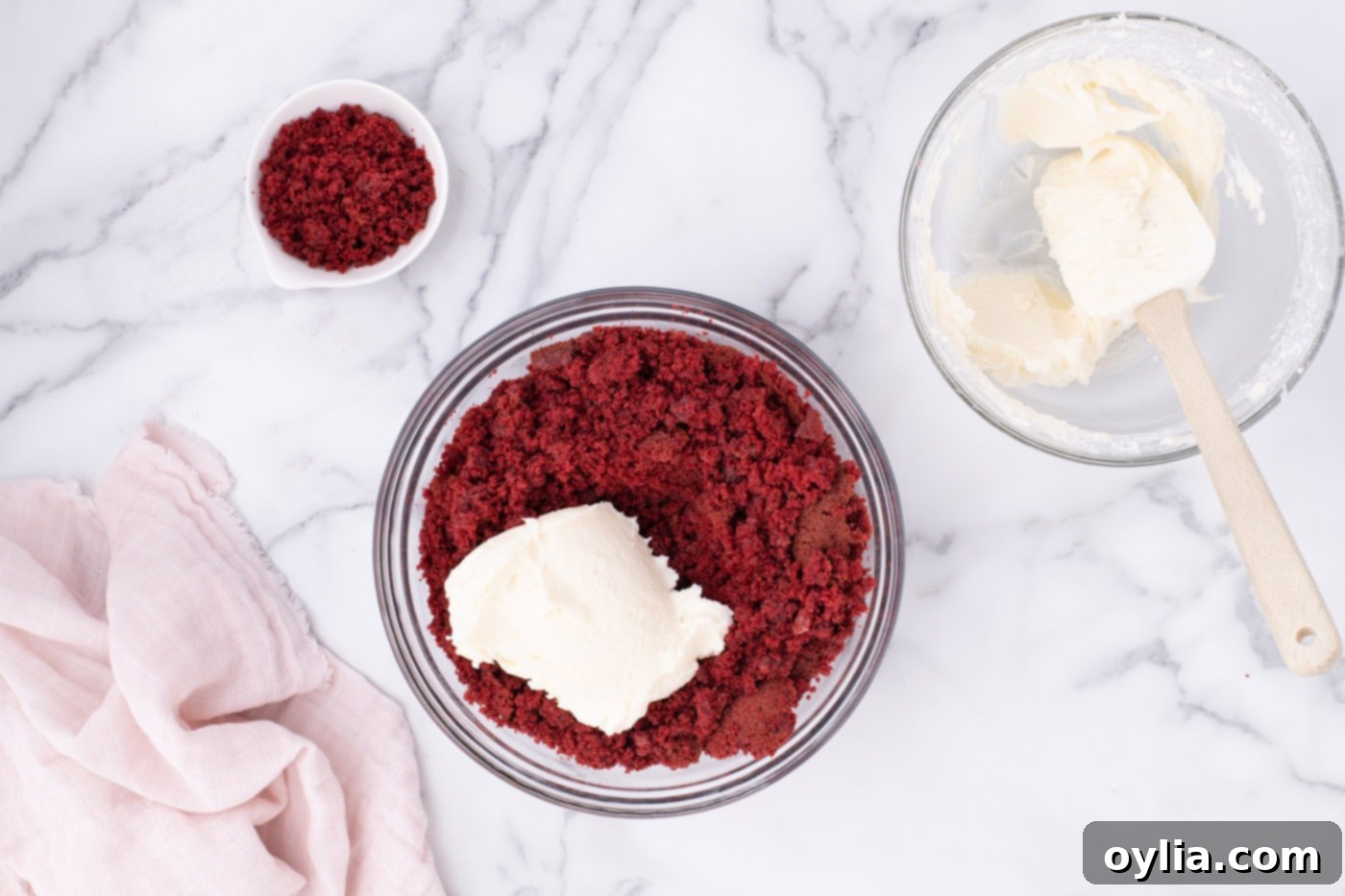 Cream cheese frosting being mixed into crumbled red velvet cake in a large bowl