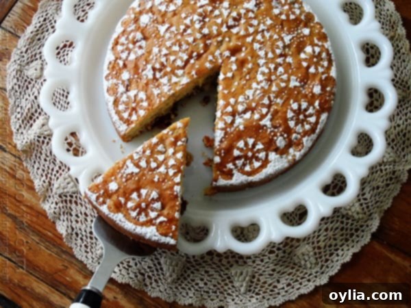 An overhead shot of a freshly baked Merryfield apple cake on a white platter, with a single slice being carefully removed, revealing the moist interior.