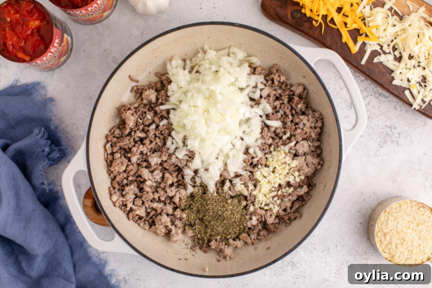 Chopped onion, minced garlic, and Italian seasoning being added to the browned beef and sausage mixture in the skillet.