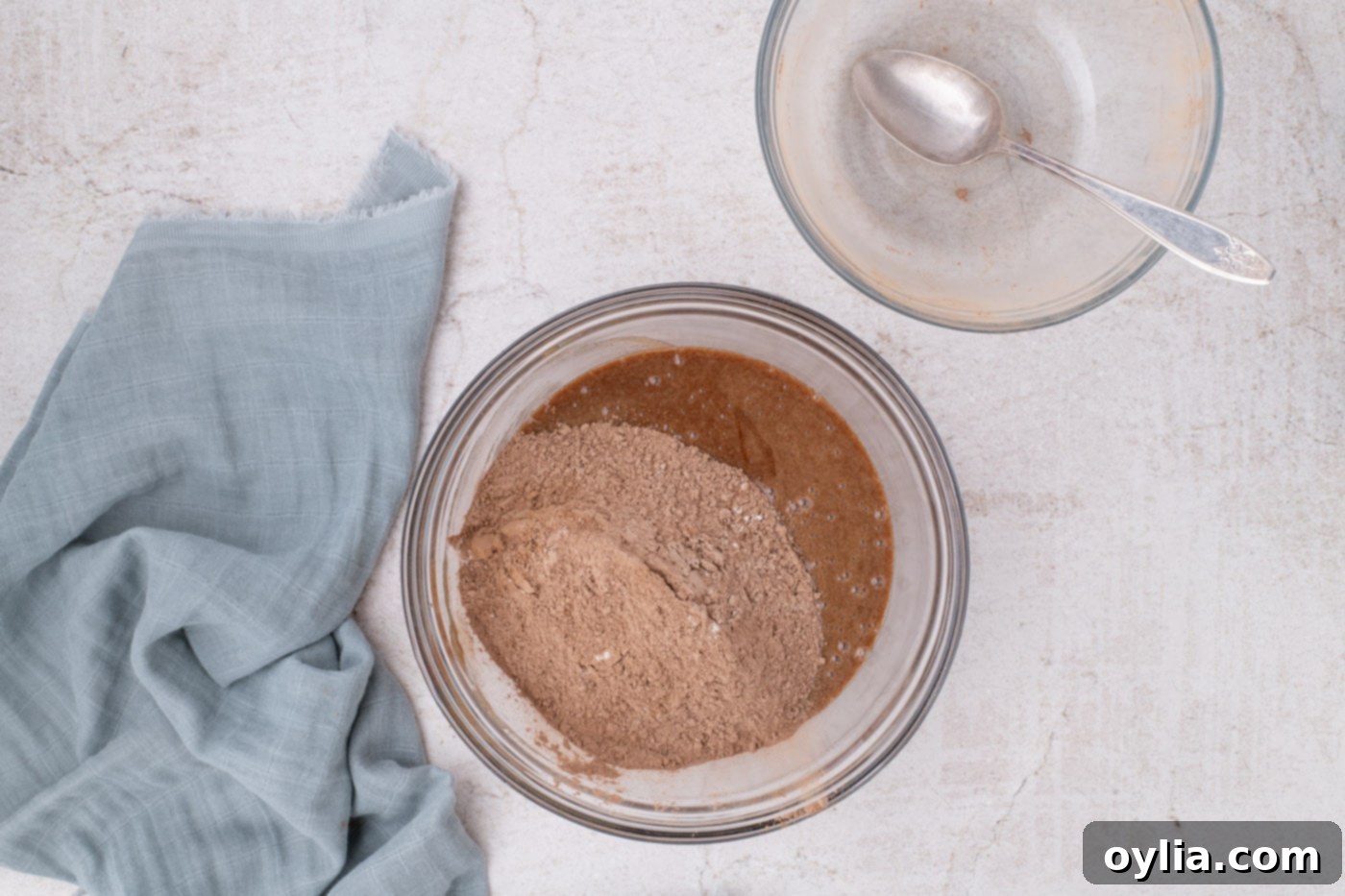 Folding the sifted dry ingredients (flour, cocoa, salt) into the wet brownie batter with a silicone spatula.