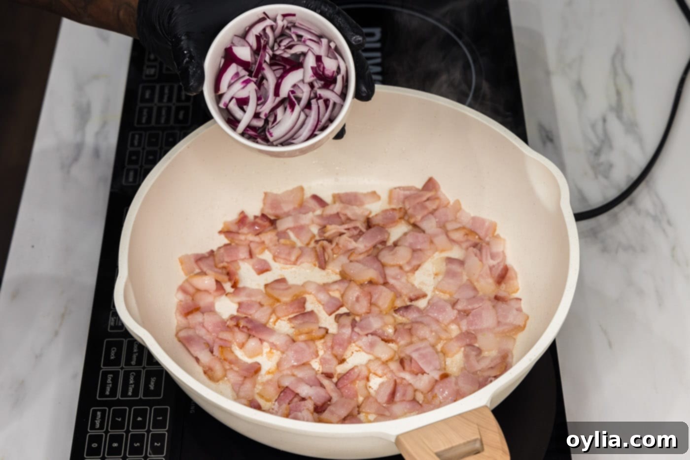 adding sliced onion to pan of partially cooked bacon, cooking together.