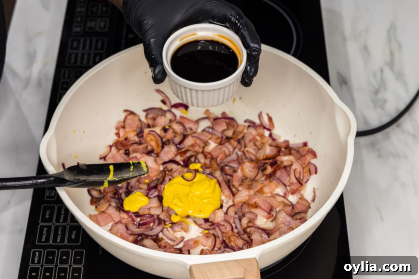 adding soy sauce to skillet with bacon, mustard, and onions, creating a rich sauce.