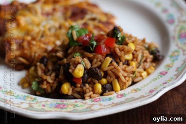 A close up photo of Spanish rice with black beans and corn, garnished with cilantro and fresh tomatoes.