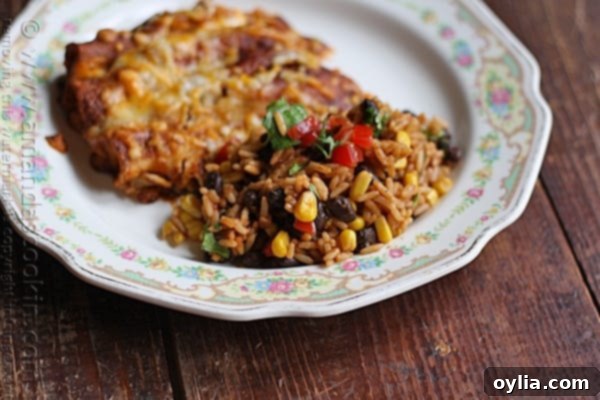 A close up photo of Spanish rice with black beans and corn on a white plate, with blurred enchiladas in the background.