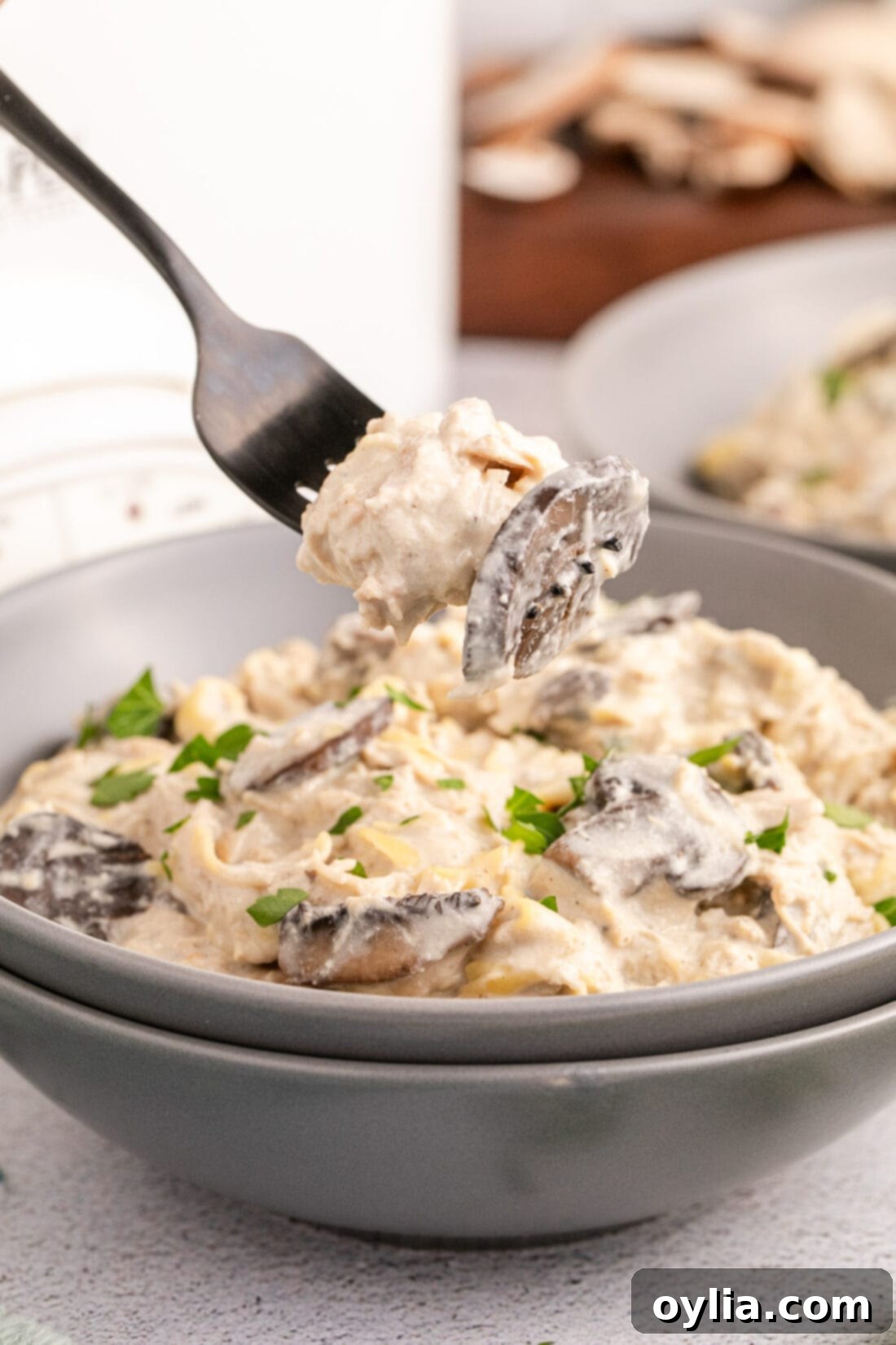 A fork lifting a spoonful of Slow Cooker Chicken Stroganoff from a bowl, showcasing its creamy texture.