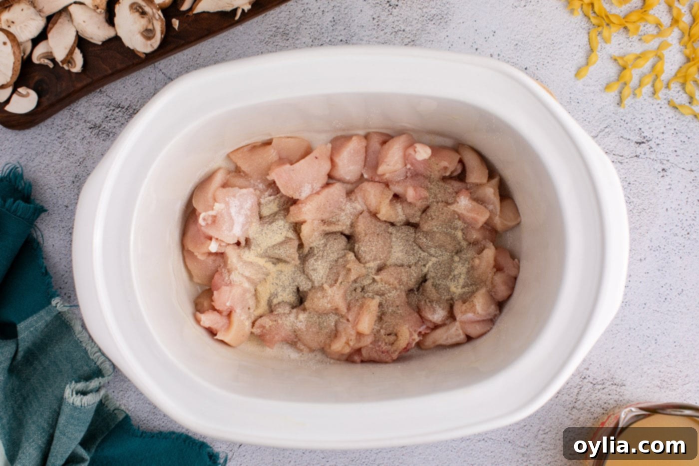 Cubed chicken in a crock pot seasoned with salt, pepper, and onion powder.