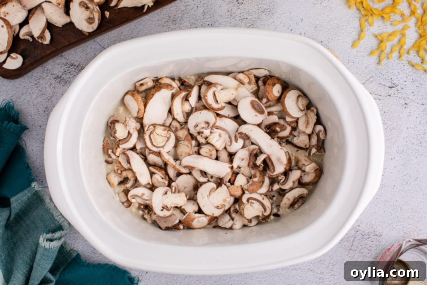 Sliced mushrooms added on top of the chicken and sauce mixture in the slow cooker.
