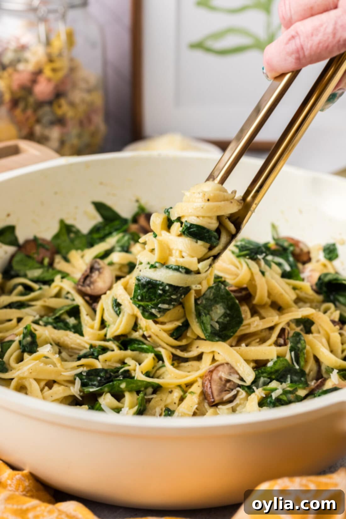 Fresh Spinach Fettuccine 2 Spinach Fettuccine wrapped around a pair of tongs being lifted out of a skillet, showcasing the pasta, spinach, and mushrooms