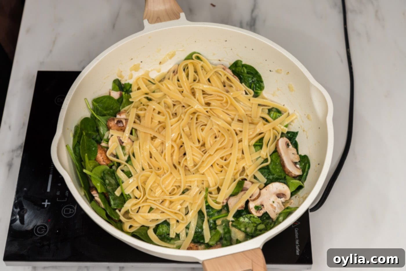 Cooked fettuccine noodles being added to the spinach and mushroom mixture in a skillet