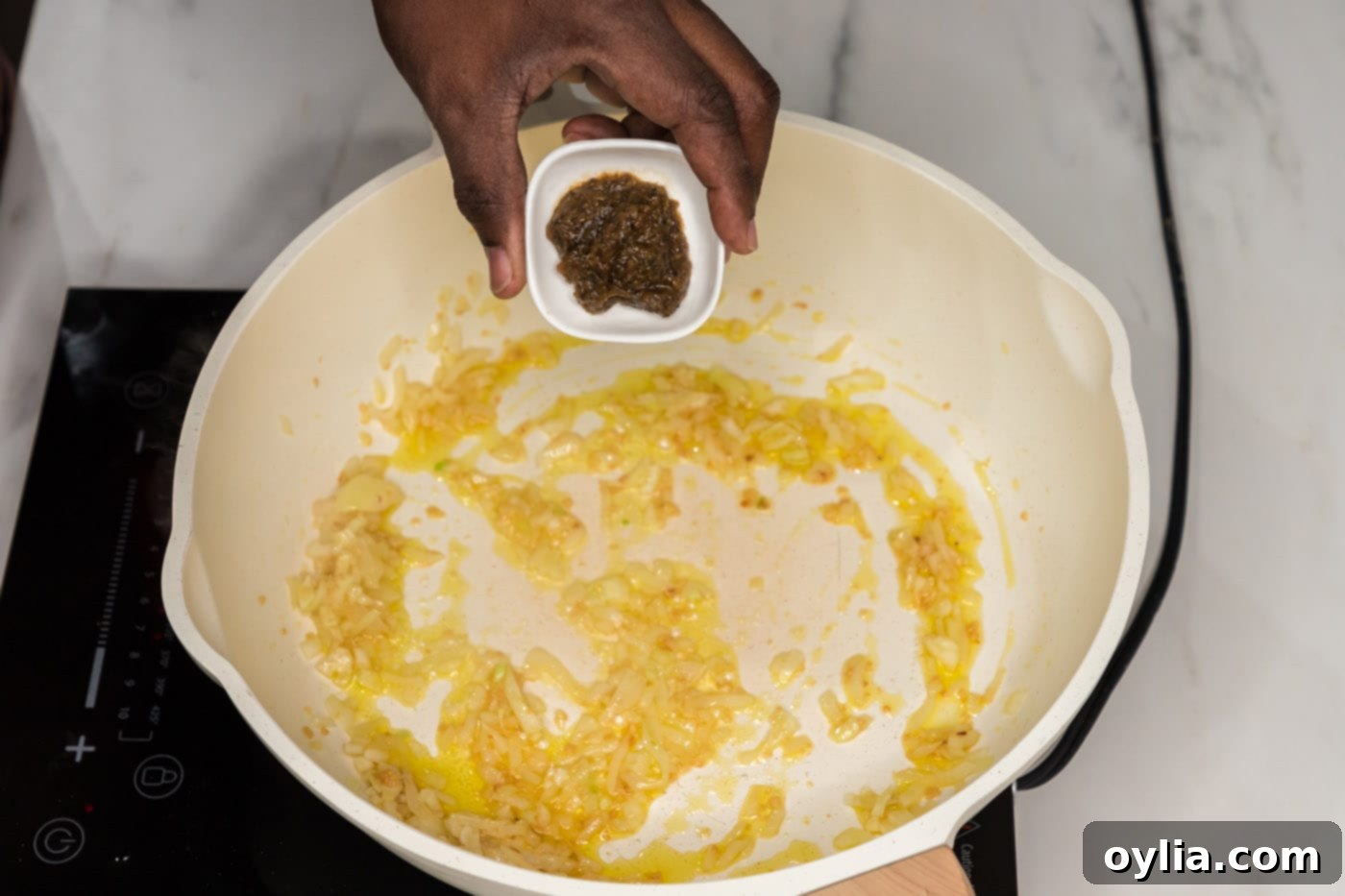 Adding bouillon base to a skillet with sautéed onion and garlic for the pasta sauce