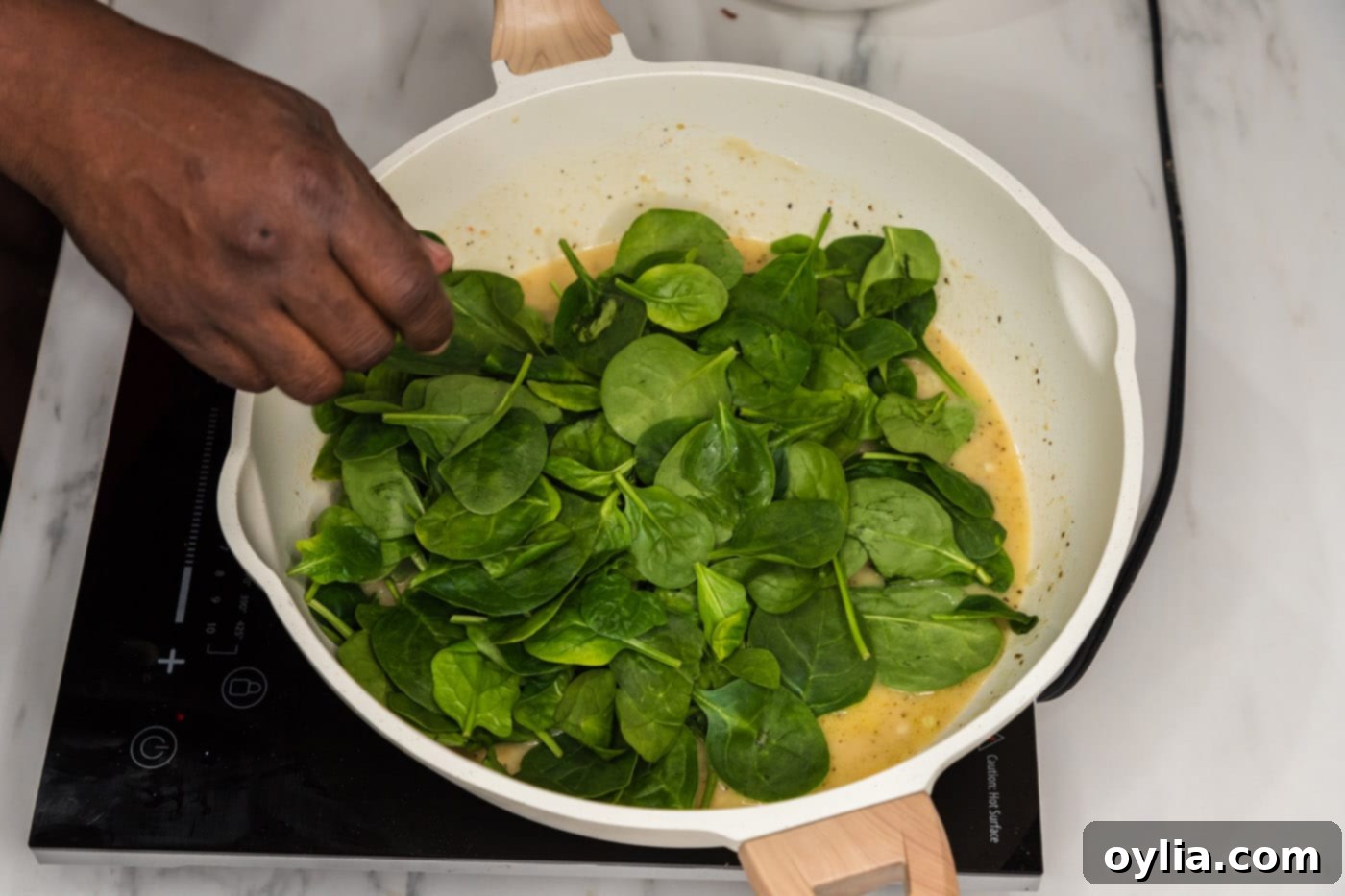 Fresh spinach leaves wilting into the pasta sauce in a skillet