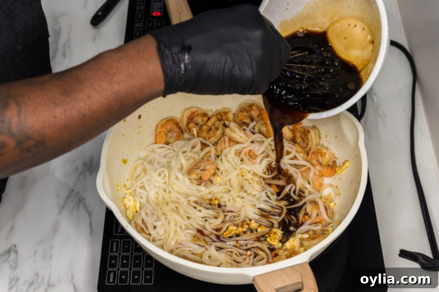 pouring pad thai sauce into skillet with rice noodles and shrimp