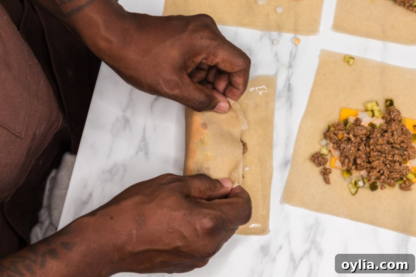 Hands demonstrating the technique of rolling an egg roll wrapper over its filling.
