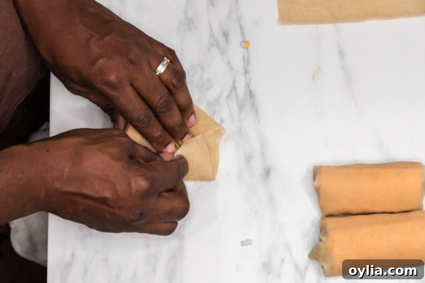 Hands completing the roll of an egg roll wrapper, ensuring a tight seal.