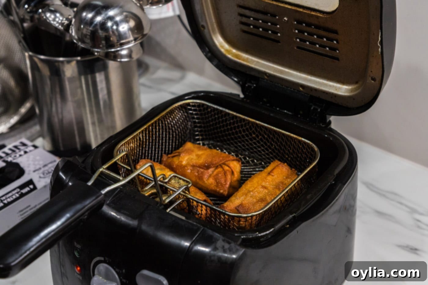 Crispy, golden-brown egg rolls in a deep fryer basket, lifted out of the oil.