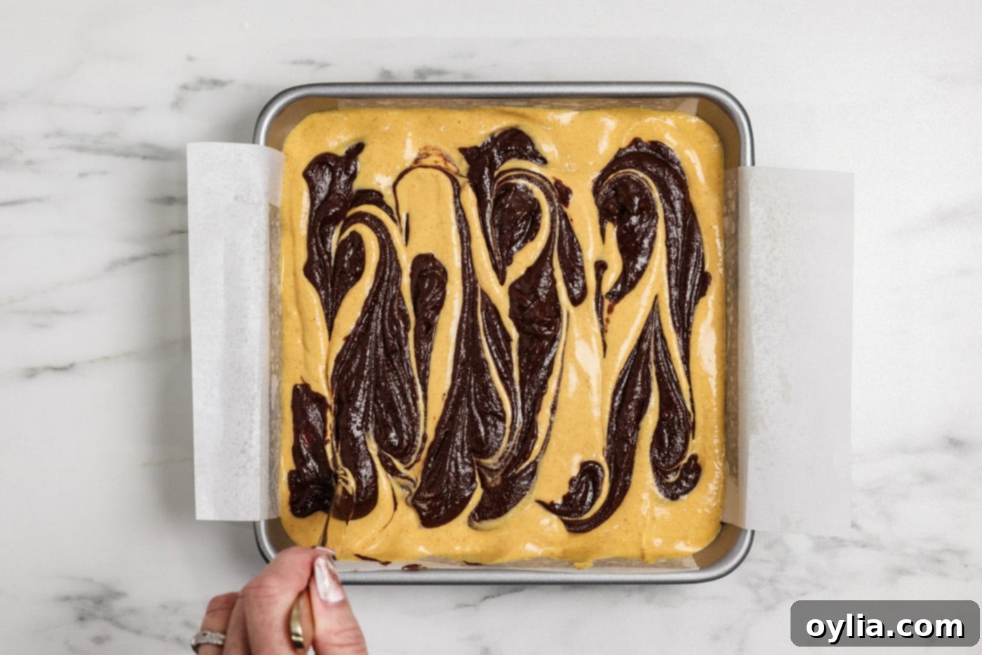 Spiced Pumpkin Swirl Cheesecake Brownies 14 Hand using a butter knife to create swirls in the brownie and cheesecake batters