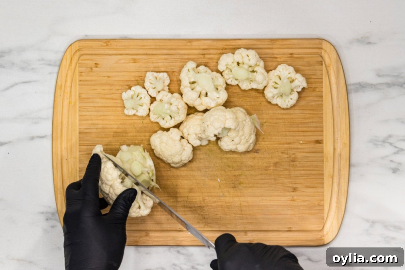 Hand using a knife on a cutting board to cut cauliflower head into florets
