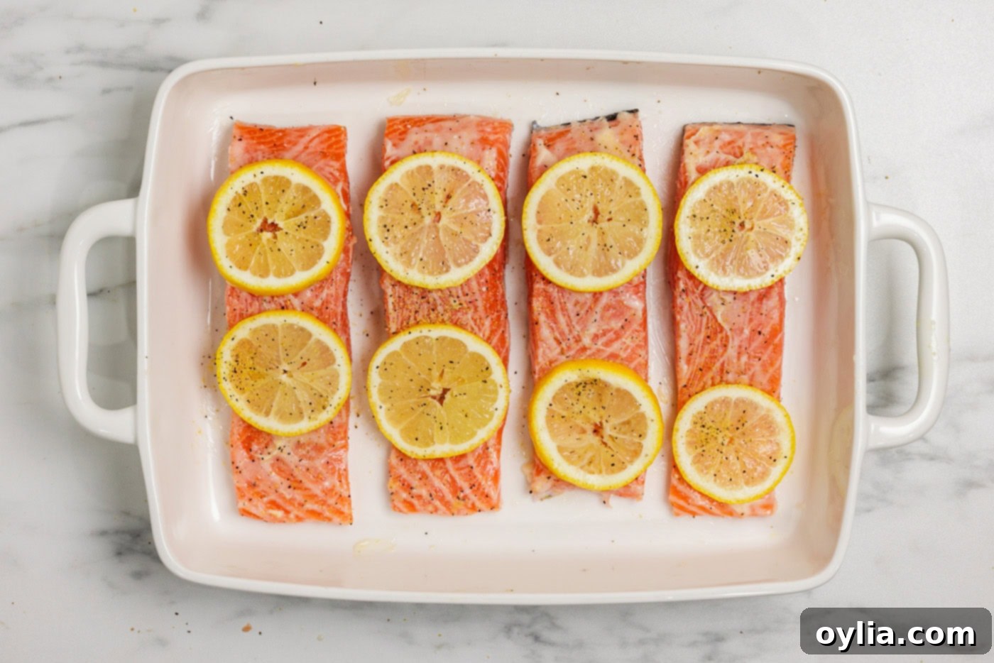 Zesty Baked Salmon 6 salmon filets topped with lemon butter and sliced lemons in a baking dish