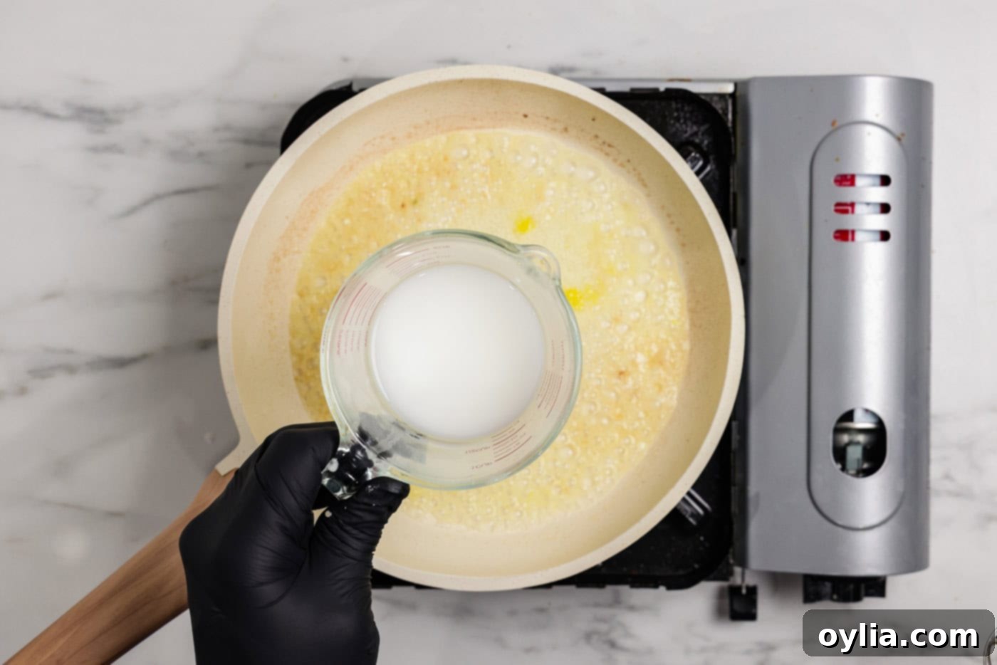 Zesty Baked Salmon 7 hand holding measuring cup of cornstarch slurry over a skillet of lemon butter sauce
