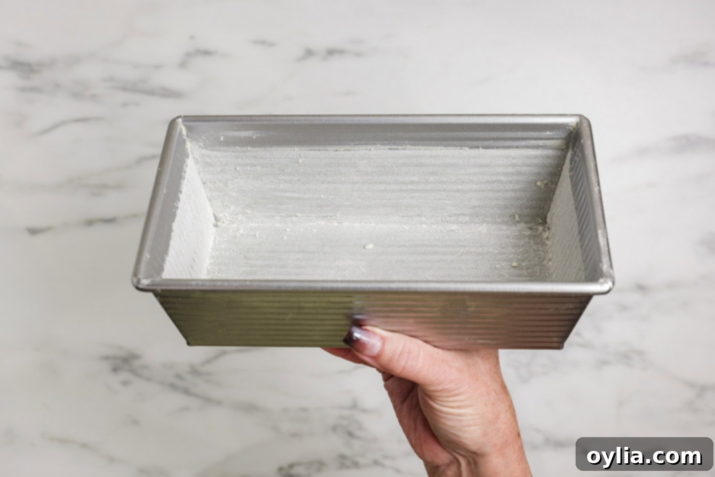 hand holding a greased and flour loaf pan ready for pumpkin banana bread batter
