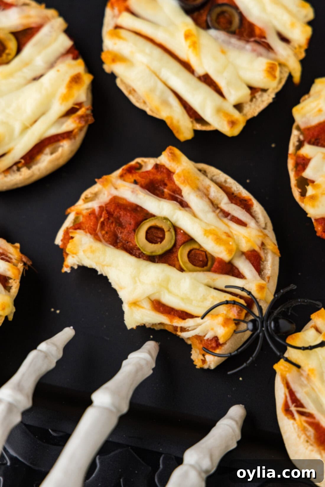 Mummy Pizza Bites 3 A half-eaten Mini Mummy Pizza on a sleek black platter, highlighting the perfect toast and melted cheese, making it an irresistible Halloween snack.