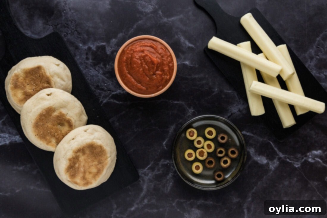 Mummy Pizza Bites 4 A colorful array of ingredients for Mini Mummy Pizzas, including English muffins, pizza sauce, olives, and string cheese, laid out on a wooden cutting board.
