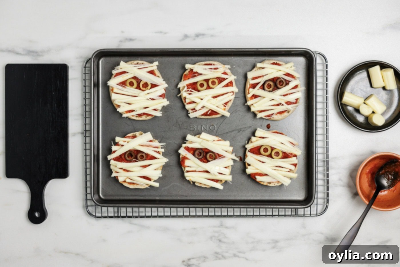 Mummy Pizza Bites 8 Mini Mummy Pizzas with string cheese strips arranged in a criss-cross pattern over pizza sauce and olive eyes, creating the mummy effect.