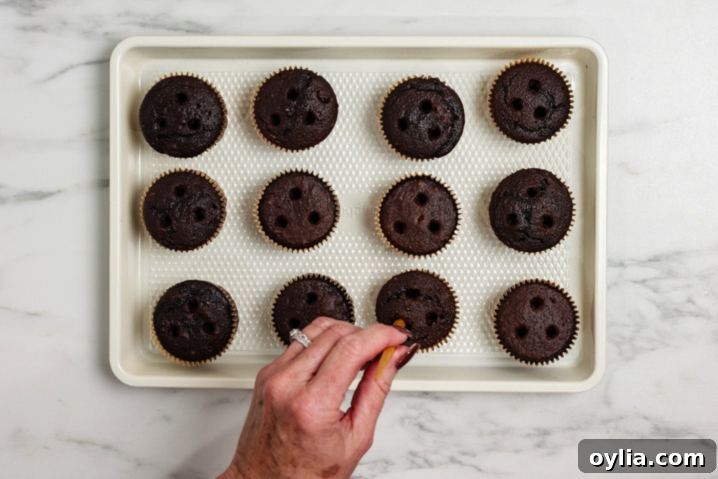 Using a skewer to poke three holes into the top of baked chocolate cupcakes